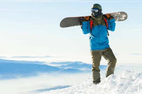 Snowboarder parado en la cima de una montaña y celebración de snowboard a la espalda —  Fotos de Stock