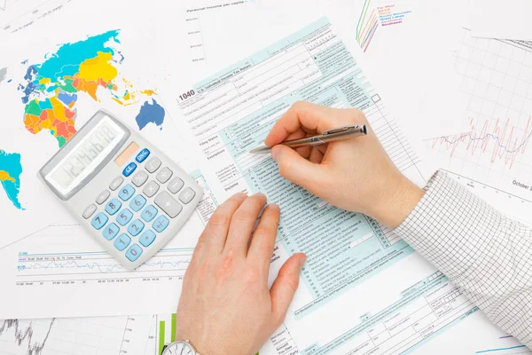 Uomo di affari compilando 1040 noi modulo fiscale con calcolatrice accanto alla mano sinistra — Foto Stock