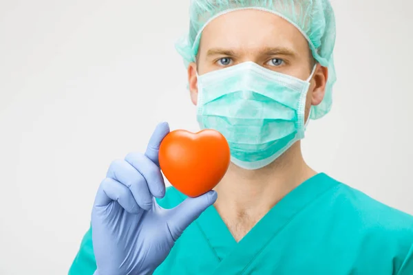 Medicina e saúde - cirurgião de uniforme verde segurando coração de brinquedo com uma mão — Fotografia de Stock