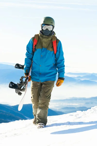 Jonge snowboarder wandelen op de top van een besneeuwde berg — Stockfoto