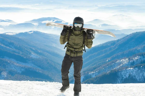 Joven snowboarder celebración de snowboard sobre sus hombros y caminar a la cima de una montaña —  Fotos de Stock