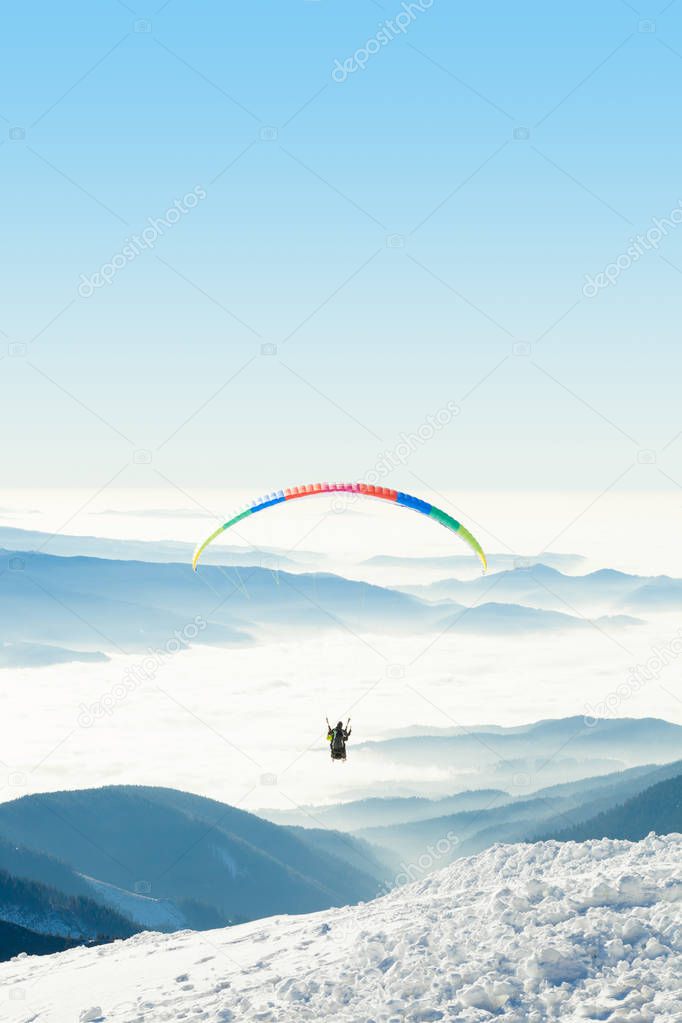Paraglider in the sky above a snowy mountain top