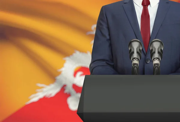 Uomo d'affari o politico fa discorso da dietro un pulpito con la bandiera nazionale sulla priorità bassa - Bhutan — Foto Stock