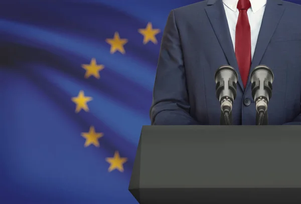 Biznesmen lub polityk przemawiający zza ambony z flagą narodową na tle kraju - Unia Europejska — Zdjęcie stockowe