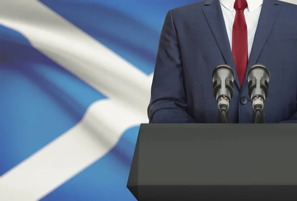 Businessman or politician making speech from behind a pulpit with national flag on background - Scotland — Stock Photo, Image