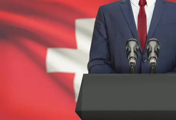 Businessman or politician making speech from behind a pulpit with national flag on background - Switzerland — Fotografia de Stock