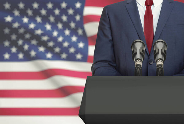 Businessman or politician making speech from behind a pulpit with national flag on background - United States