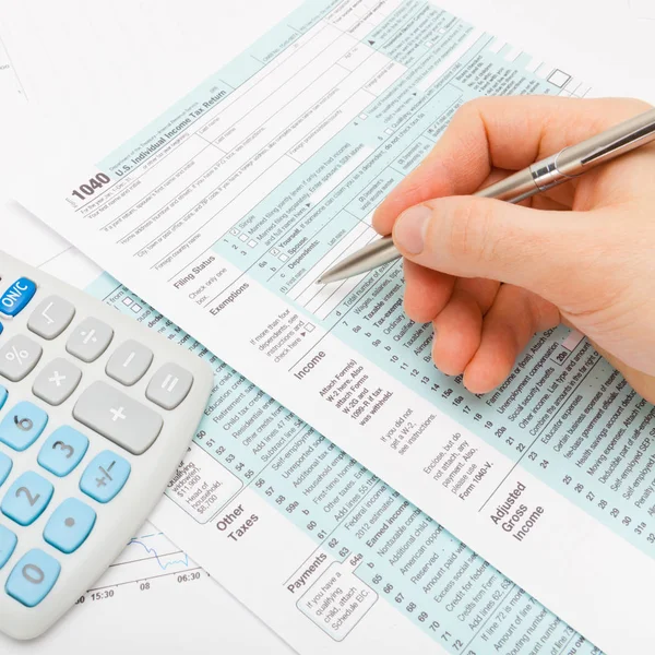 Close up shot of a male filling out US 1040 Tax Form with calculator next to it - close up studio shot — Stock Photo, Image