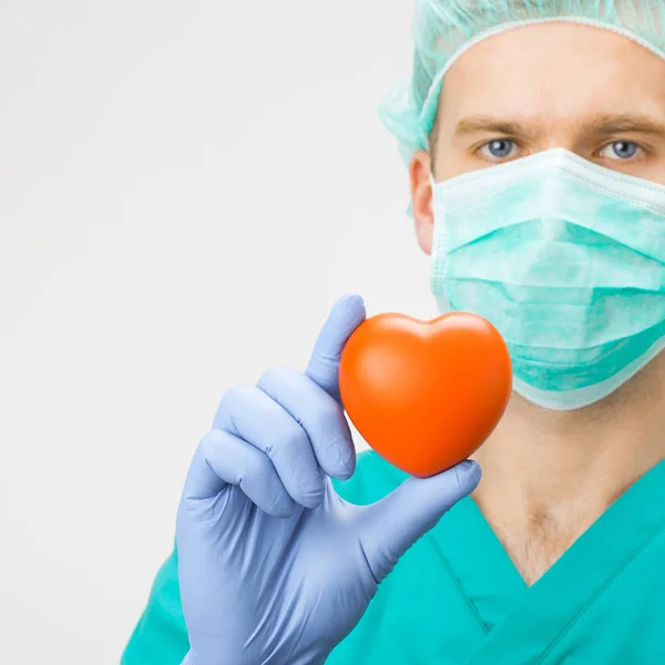 Surgeon in green uniform holding toy heart in hand - medicine and healthcare symbols — Stock Photo, Image