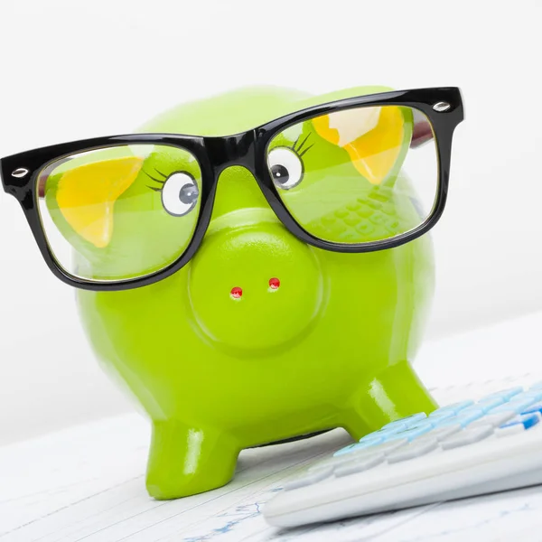 Piggy bank in glasses next to a calculator - close up studio shot — Stock Photo, Image