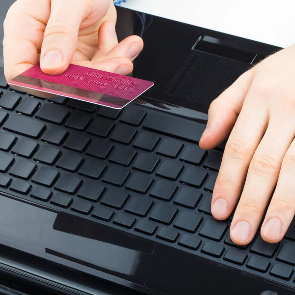 Man holding a credit card next to computer keyboard and trying to do online payment - close up studio shot — Stock Photo, Image