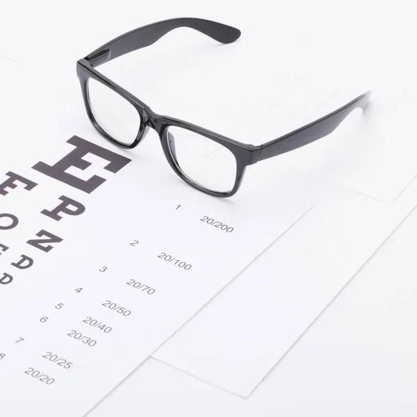 Medicine and medical symbols - close up studio shot of a table for eyesight test with glasses over it — Stock Photo, Image
