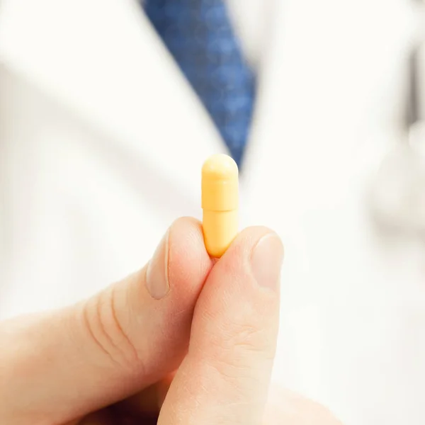 Medizin und medizinische Symbole - Arzt hält Pille gelbe Farbe mit zwei Fingern — Stockfoto