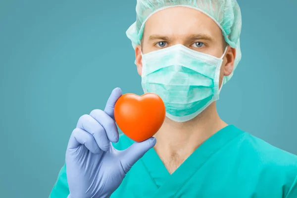 Medicine and healthcare - surgeon in green uniform holding toy heart on light blue background — Stock Photo, Image