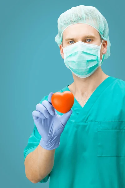 Medizin und Pflege - Chirurg hält Spielzeug Herz mit einer hand auf hellblauem Hintergrund — Stockfoto