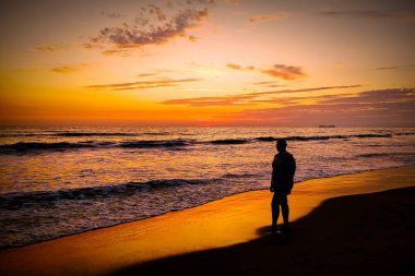 Sahilde gün batımını izleyen kişi.