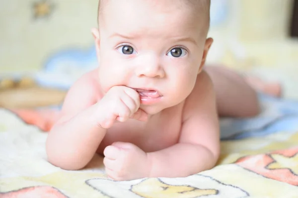 the baby is lying on a yellow blanket and chewing on his finger