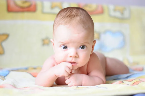 the baby is lying on a yellow blanket and chewing on his finger