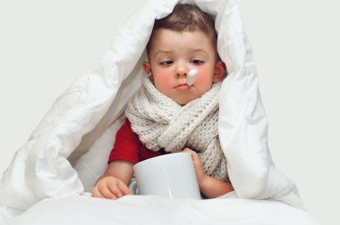 Küçük tatlı bir çocuk hastalanıyor ve ısıyı ağız termometresiyle ölçüyor ve boynunda büyük bir örgü eşarp ile battaniyeyle oturuyor. Gözlerini kısarak termometreye bakıyor.