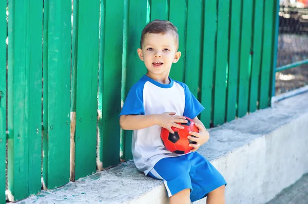 彼の赤いサッカーボールと青いサッカーの制服を着た小さな3歳の少年 — ストック写真