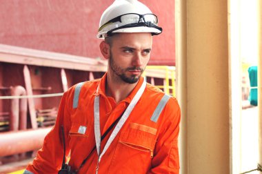 Turuncu tulumlu deneyimli bir denizci ve beyaz kasklı bir gemi gemisinde çalışıyor..