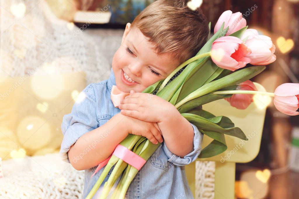 Cute little boy gentleman in a blue denim shirt and peach bow tie holds a large bouquet of pink tulips