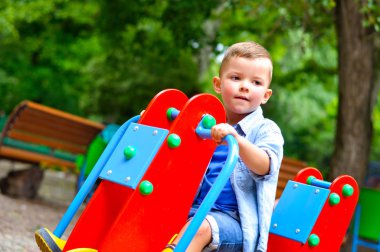 Yaz parkında salıncakta sallanan üç yaşında tatlı bir çocuk.
