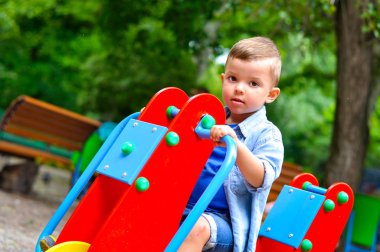 Yaz parkında salıncakta sallanan üç yaşında tatlı bir çocuk.