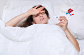 Nemocná mladá žena s teploměrem v bílé posteli.Pocit nemoci