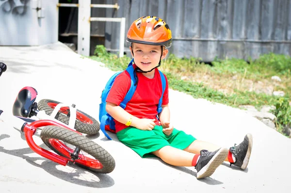 Koruyucu Kasklı Çocuk Kırmızı Beyaz Dengeli Bisikletinin Yanında Oturuyor — Stok fotoğraf