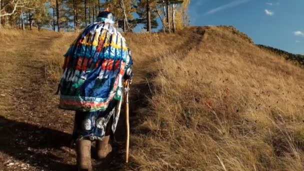 Elinde baston olan yaşlı bir şaman dağa tırmanıyor.. — Stok video