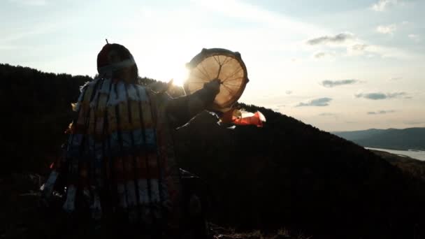 Mouvement lent de la silhouette d'un chaman avec un tambourin au coucher du soleil . — Video