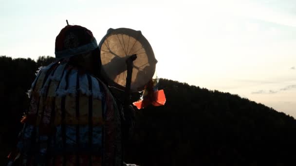 Langzame beweging van het silhouet van een sjamaan die een tamboerijn slaat bij zonsondergang. — Stockvideo