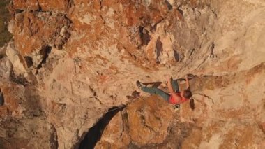 Genç cesur kadının hava görüntüsü kayaya tırmanıyor, kırılıyor, yere düşüyor ve güvenlik ipine tutunuyor. Yavaş çekim.