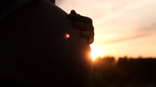 Nahaufnahme einer schwangeren Frau, die ihren Bauch bei Sonnenuntergang mit der Hand streichelt. — Stockvideo