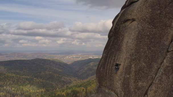 Молодой человек взбирается на вершину горы на вертикальной стене с прекрасным видом на долину . — стоковое видео