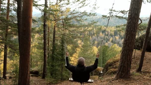 Un joven feliz se balancea en el bosque con una hermosa vista del paisaje de otoño en un desfiladero de montaña . — Vídeo de stock