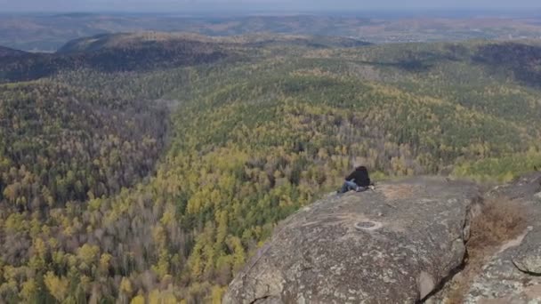 一人の男性登山家が山の上に座り、渓谷の美しい景色を楽しむ. — ストック動画