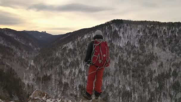 En ensam ung manlig vandrare står på toppen av ett berg vid solnedgången. — Stockvideo
