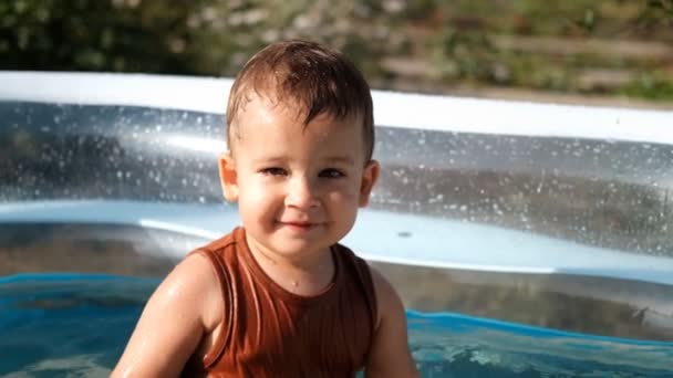 Retrato en cámara lenta del pequeño chico caucásico sentado en una piscina al aire libre . — Vídeo de stock