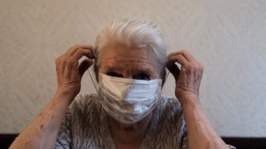 Koruyucu bir tıbbi maske takan yaşlı bir kadının yavaş çekim portresi..