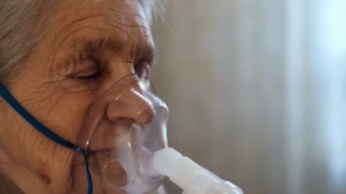 Tıbbi solunum maskesi takan, gözleri kapalı yaşlı bir kadının yakın çekimi..