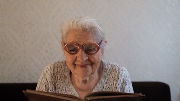 Portret starszej kobiety w okularach czytającej książkę i uśmiechającej się. — Wideo stockowe