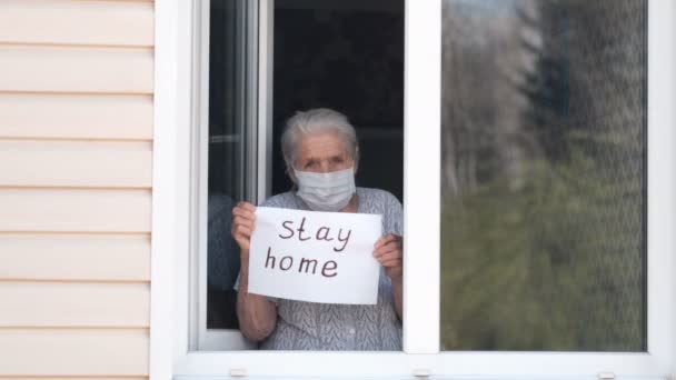 Mujer mayor sostiene un cartel con las palabras quedarse en casa — Vídeos de Stock