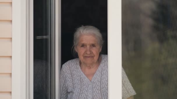 Stará žena se podívá z okna a usměje se.. — Stock video