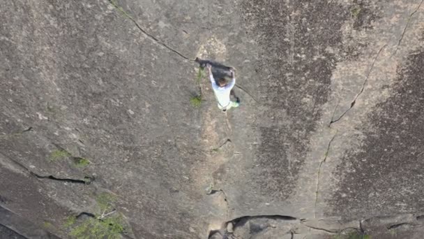 Vista superior: un joven valiente desciende por una pared de roca sin seguro . — Vídeo de stock