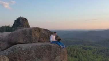 Gün batımında dağların tepesinde dizüstü bilgisayarda çalışan genç bir adamın robot görüntüsü..