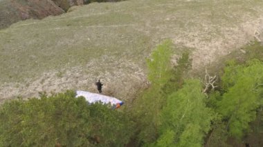 Krasnoyarsk, Rusya - 12 Mayıs 2020: Bir kayanın kenarından koşan ve zıplayan genç bir adamın hız planörünün arkasında görüntüsü.