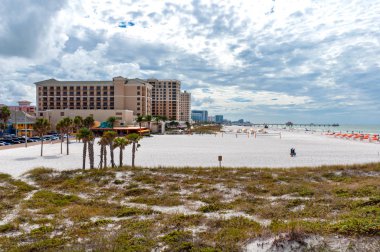 Clearwater Sahili manzaralı, modern apartman binaları, insanlar, kum tepeleri, otopark, palmiye ağaçları ve okyanus, güneşli ve bulutlu bir sabah. Florida, Usa.