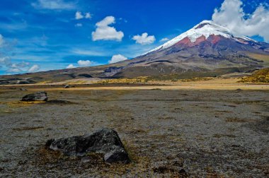 Güneşli bir sabahta, ön planda volkanik kayalar bulunan Cotopaxi volkanı manzarası. Cotopaxi Ulusal Parkı, Ekvador